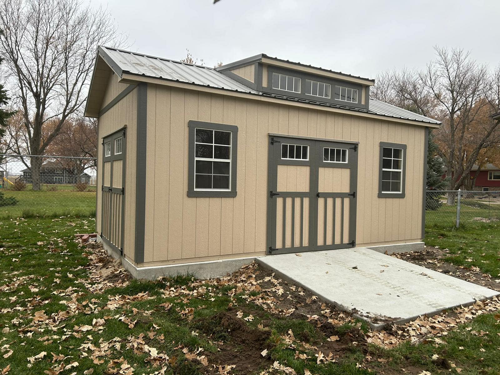 A deluxe shed with double doors on the front, two 2x3 windows on either side, and a a dormer above.