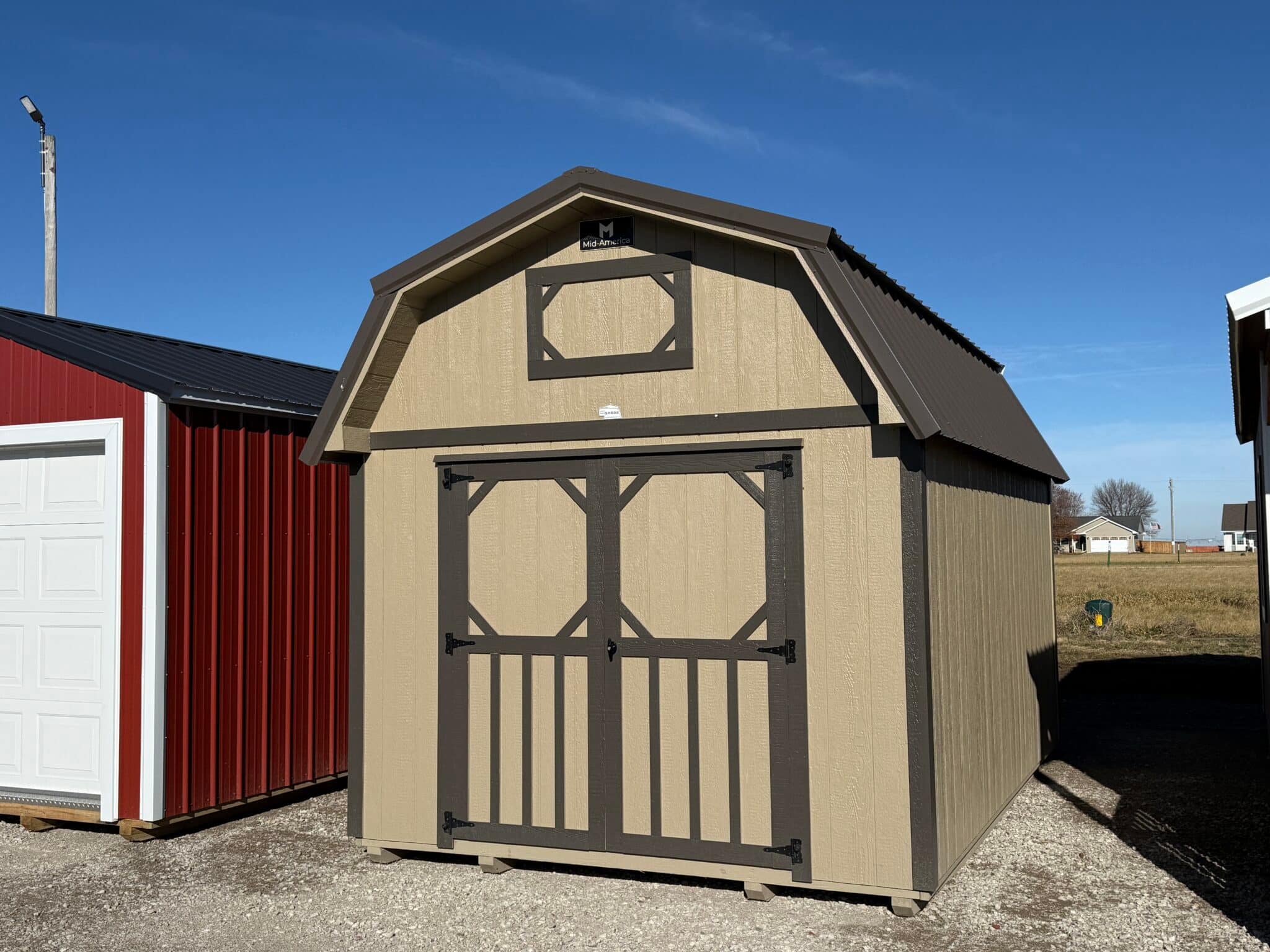 Barn-style shed with a lofted roof and double doors. The pictured shed is tan with dark brown accents.