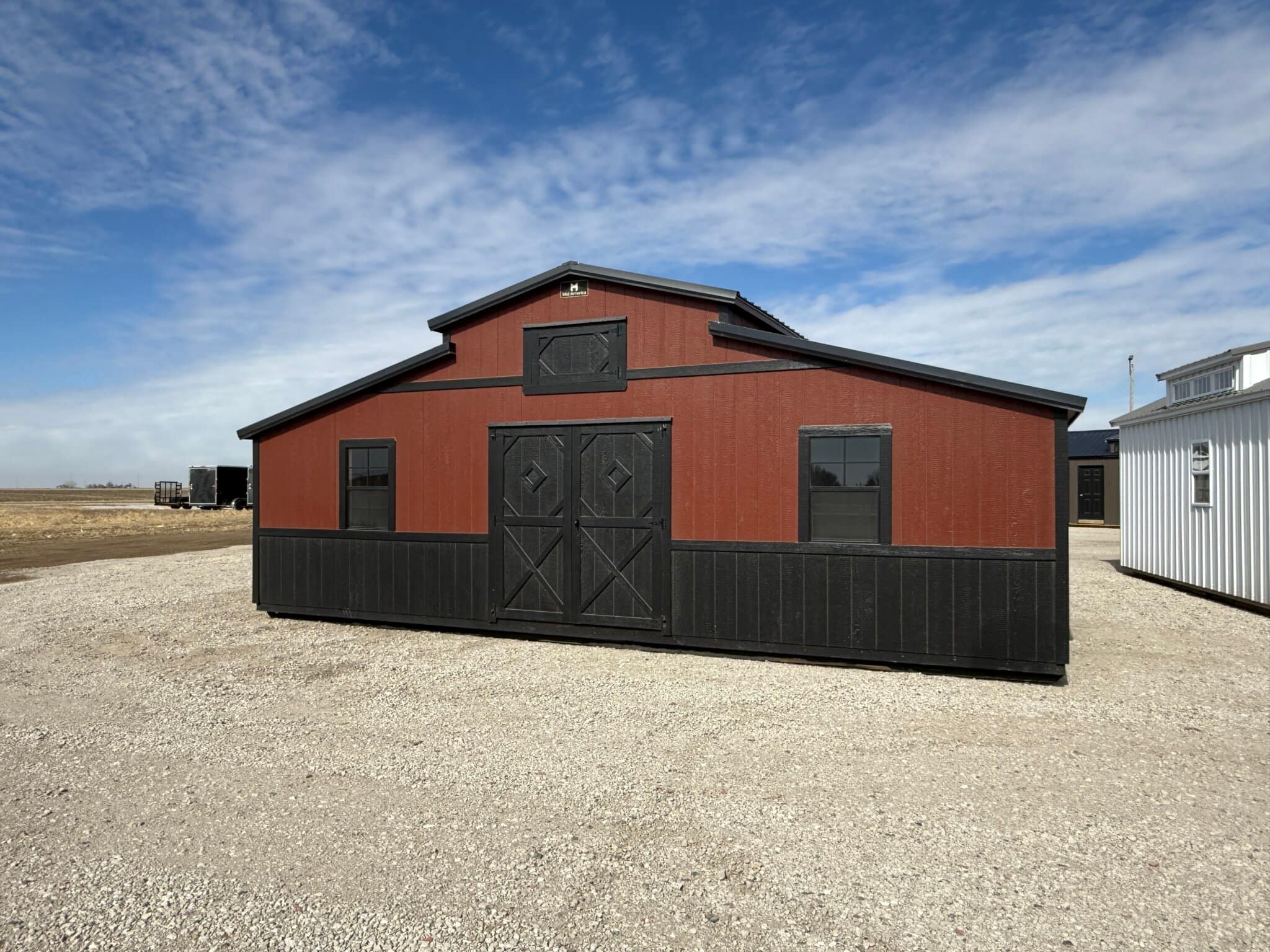 Rust red and black country-style barn on pavement slab in a sales lot.