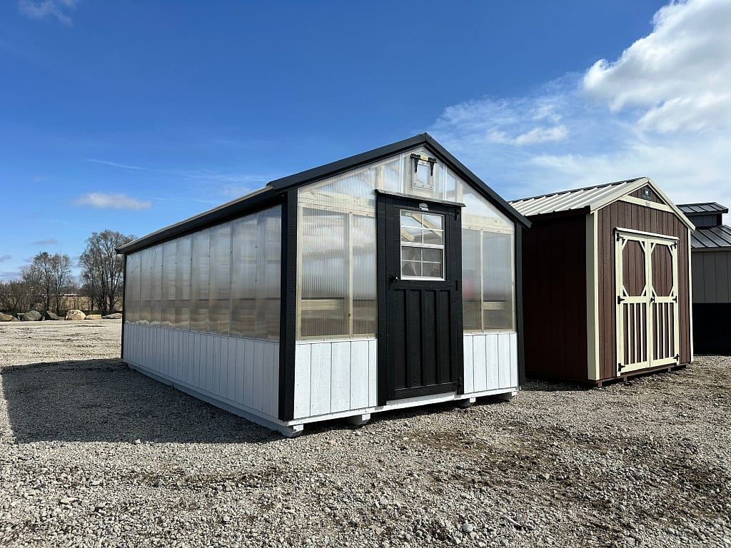 Exterior of mid-sized greenhouse, featuring polycarbonate walls and roof, with white and black accents on the building