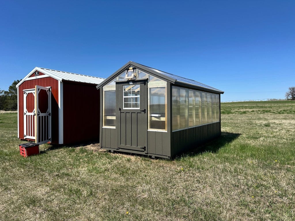 Exterior of small greenhouse with polycarbonate sides and brown trim around the base.