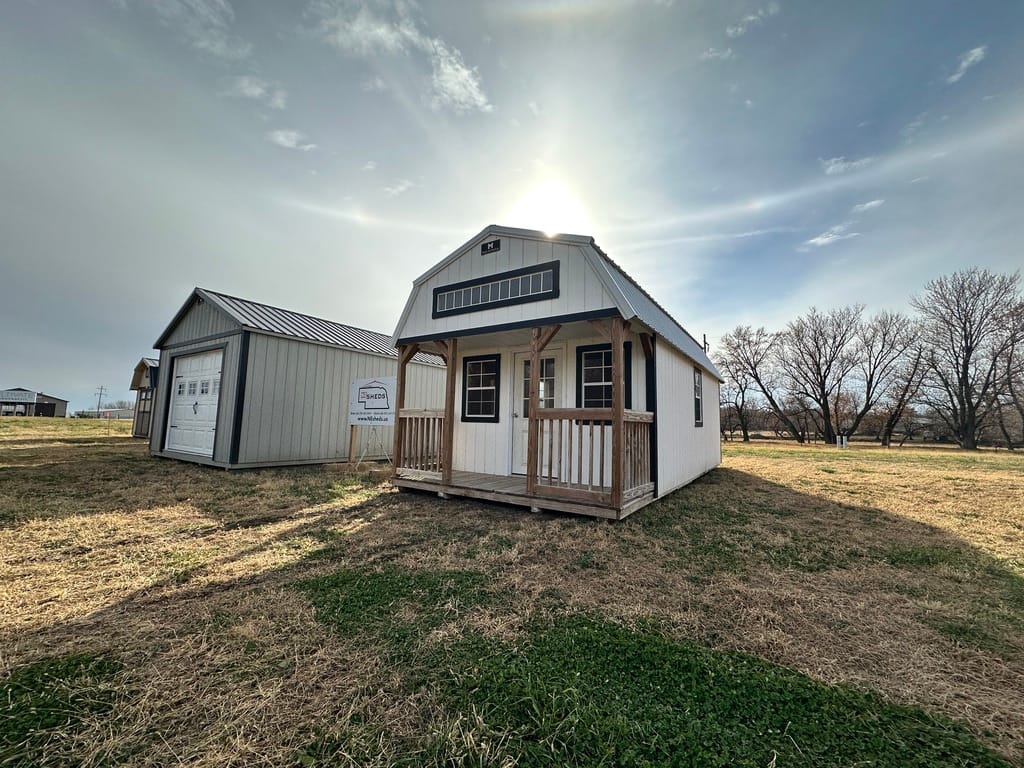 Exterior of a small white cabin, showcasing the front porch and horizontal window in lofted area.