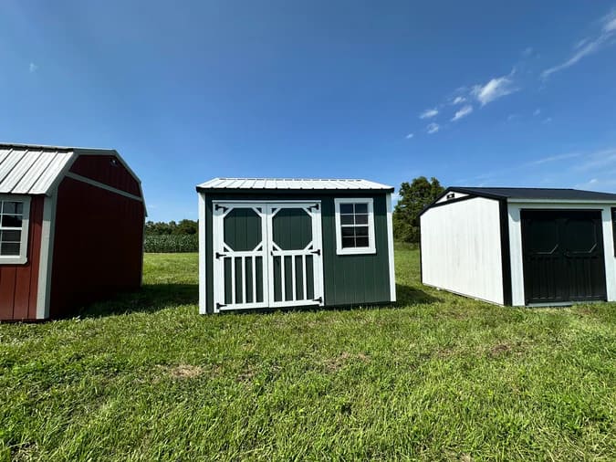 Green garden shed in lineup of other shed options. Shed is mostly forest green with white trim.